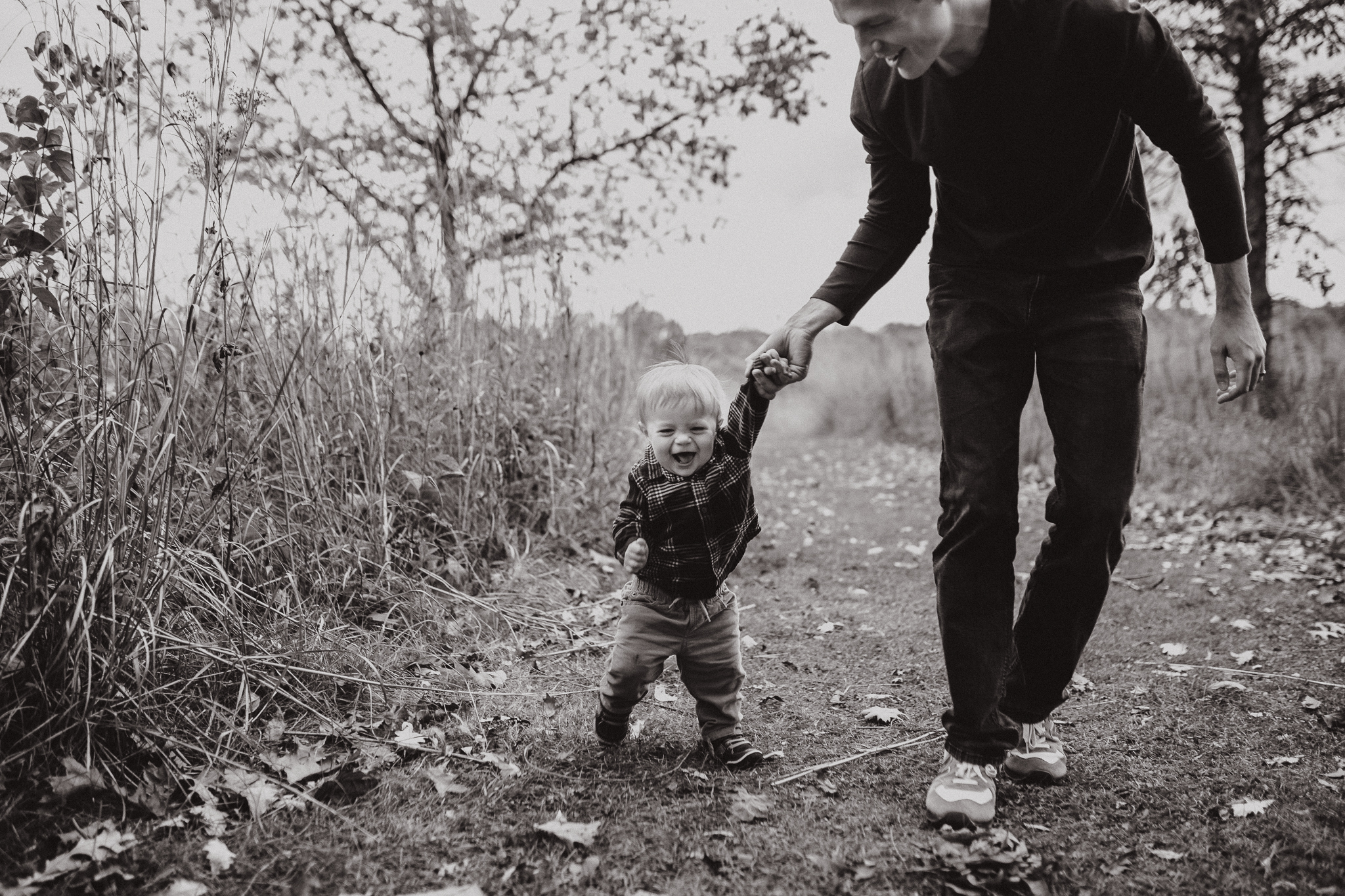 Father holding his one year old's hand as he toddles outside.