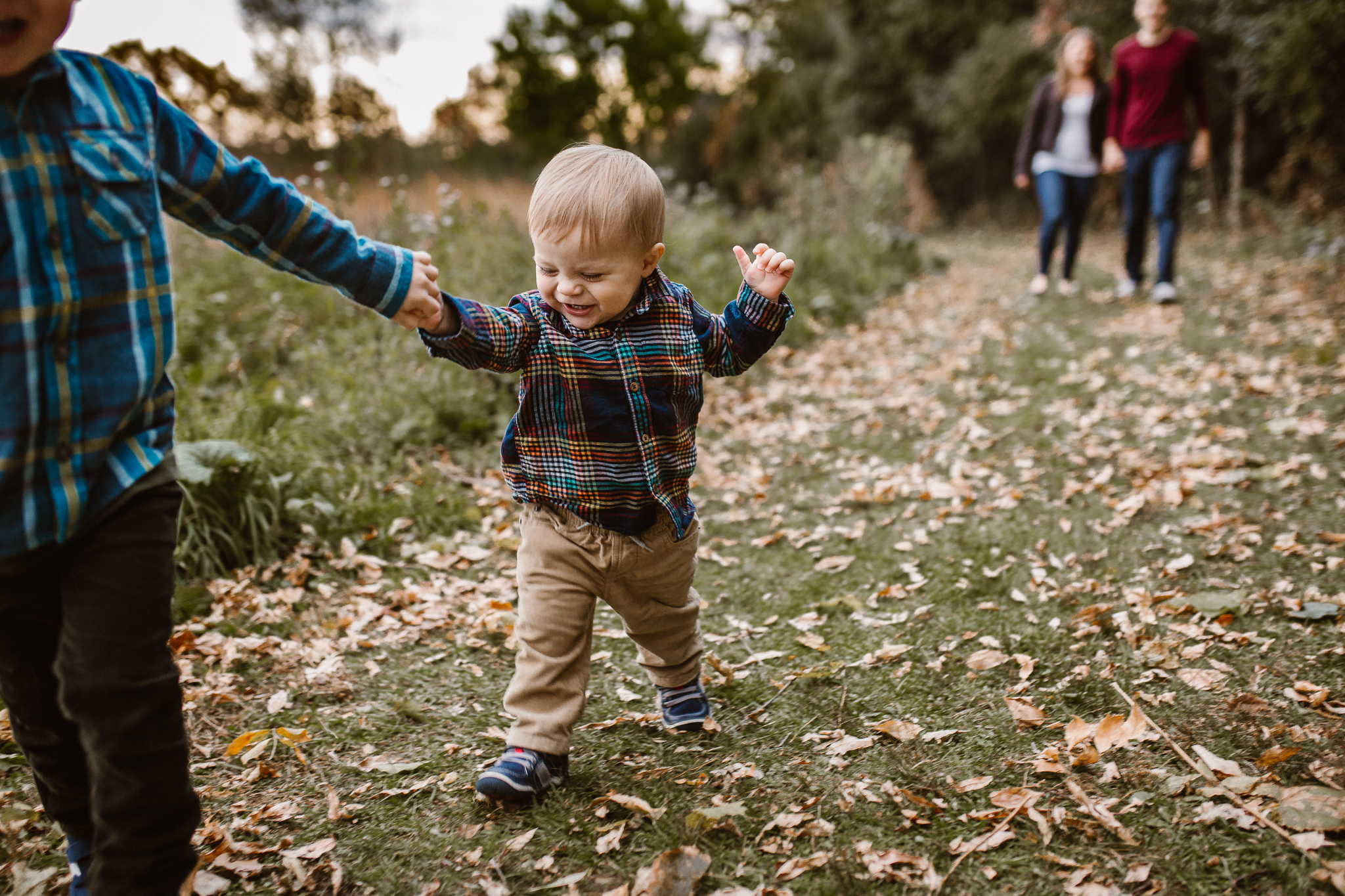 Big brother holding his younger brother's hand as they walk outside in the leaves.