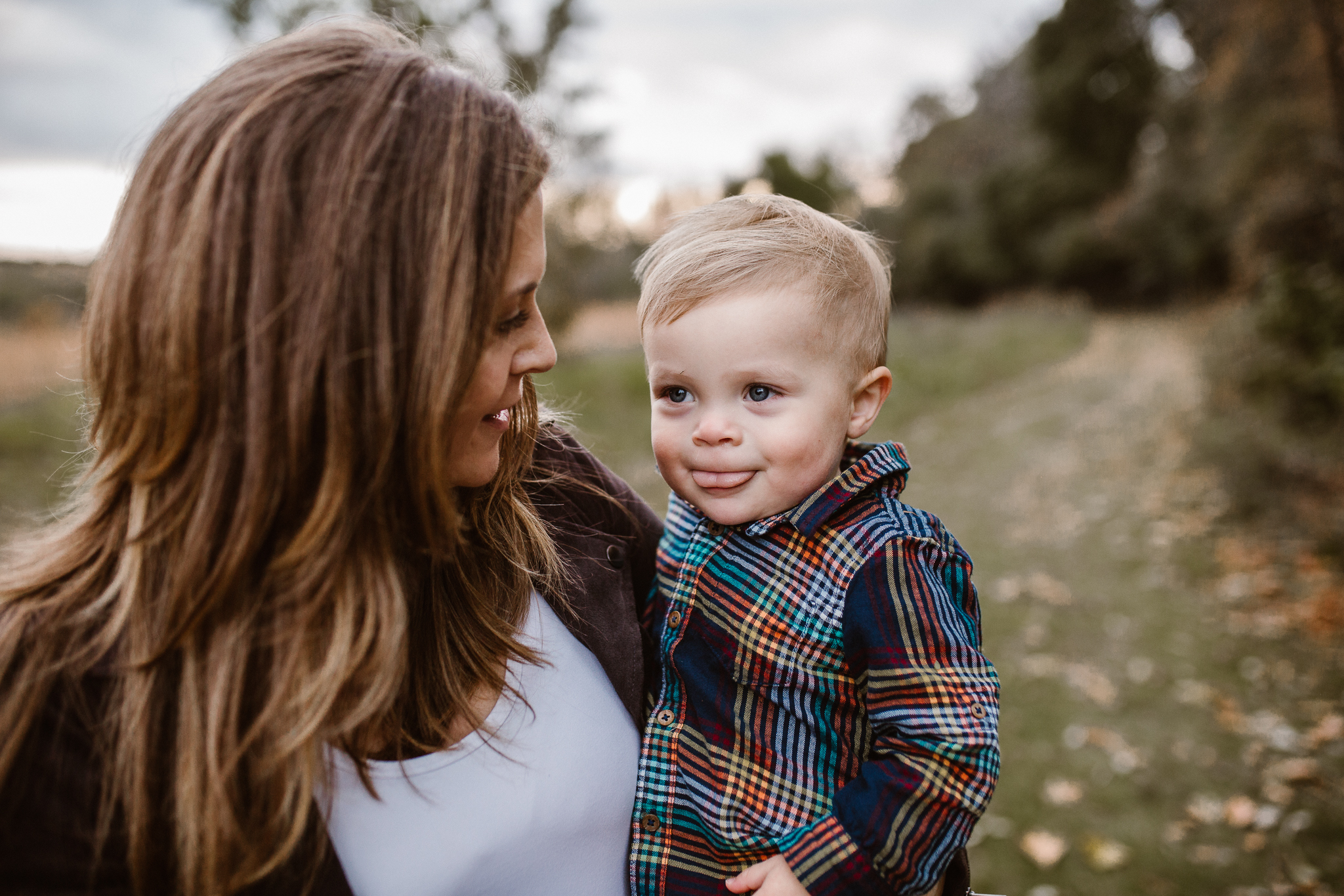 Mother holding her young son outside as he sticks his tongue out in a cute way.