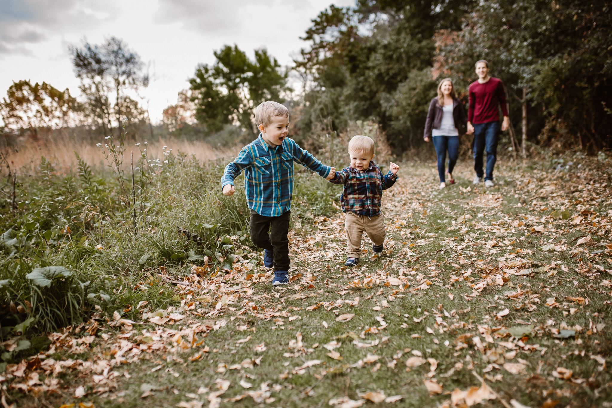 Two young brothers holding hands as they run together outside in the leaves.