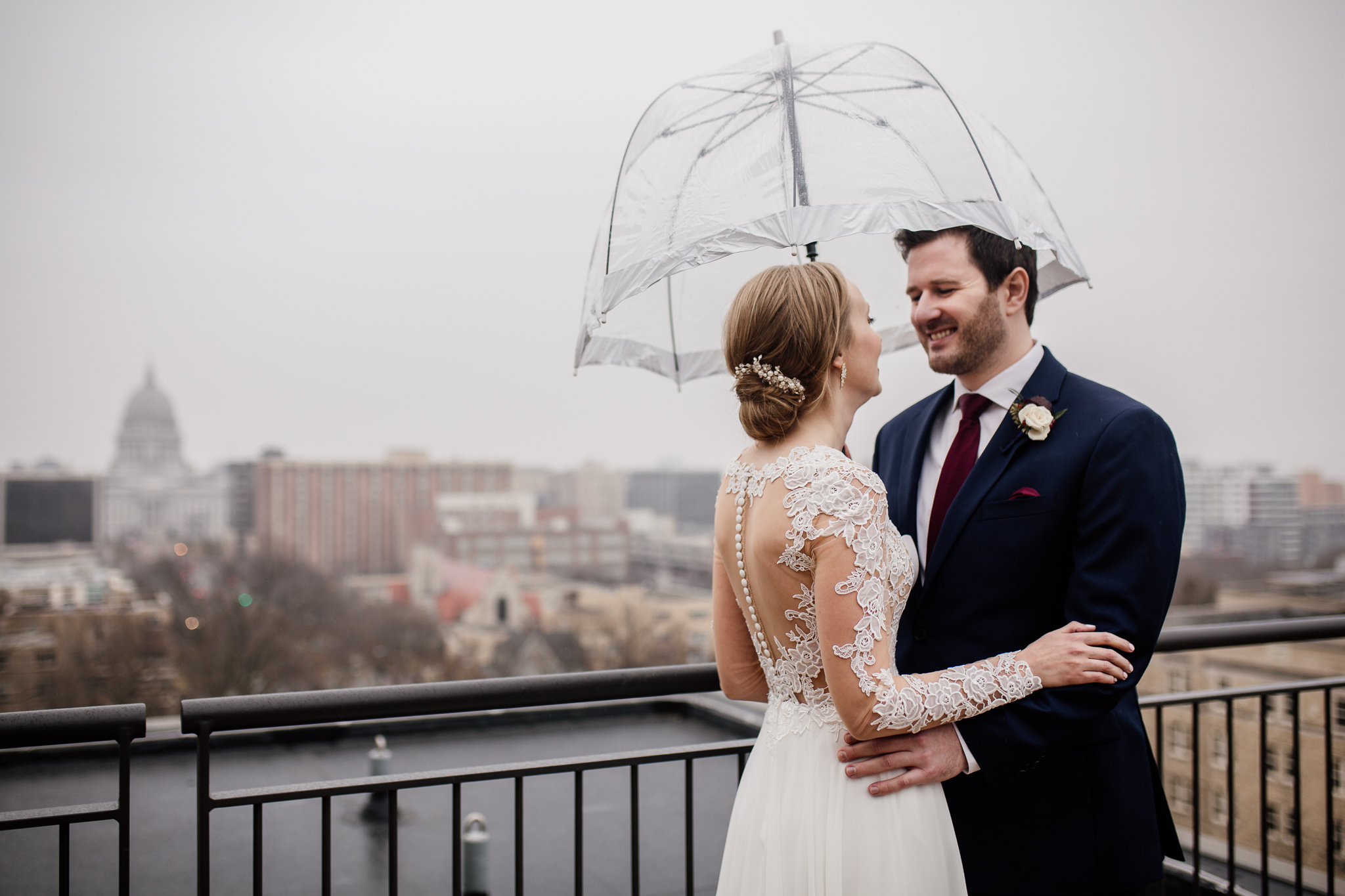 Bride and groom on the Edgewater Hotel balcony with an umbrella.