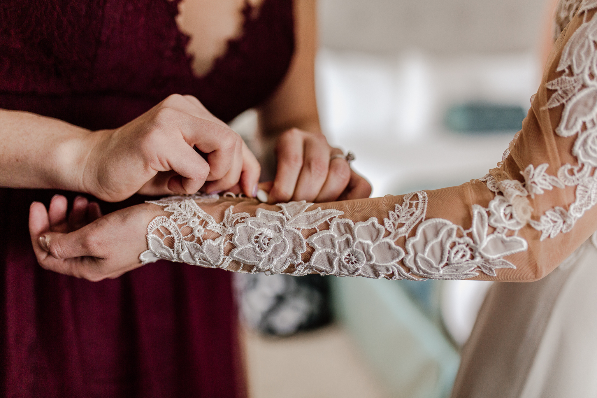 Bridesmade buttoning the bride's dress sleave.