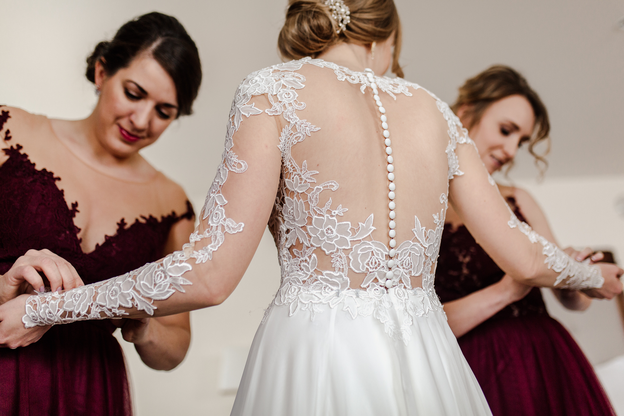 Bridesmaids buttoning the bride's dress sleaves in a hotel room.