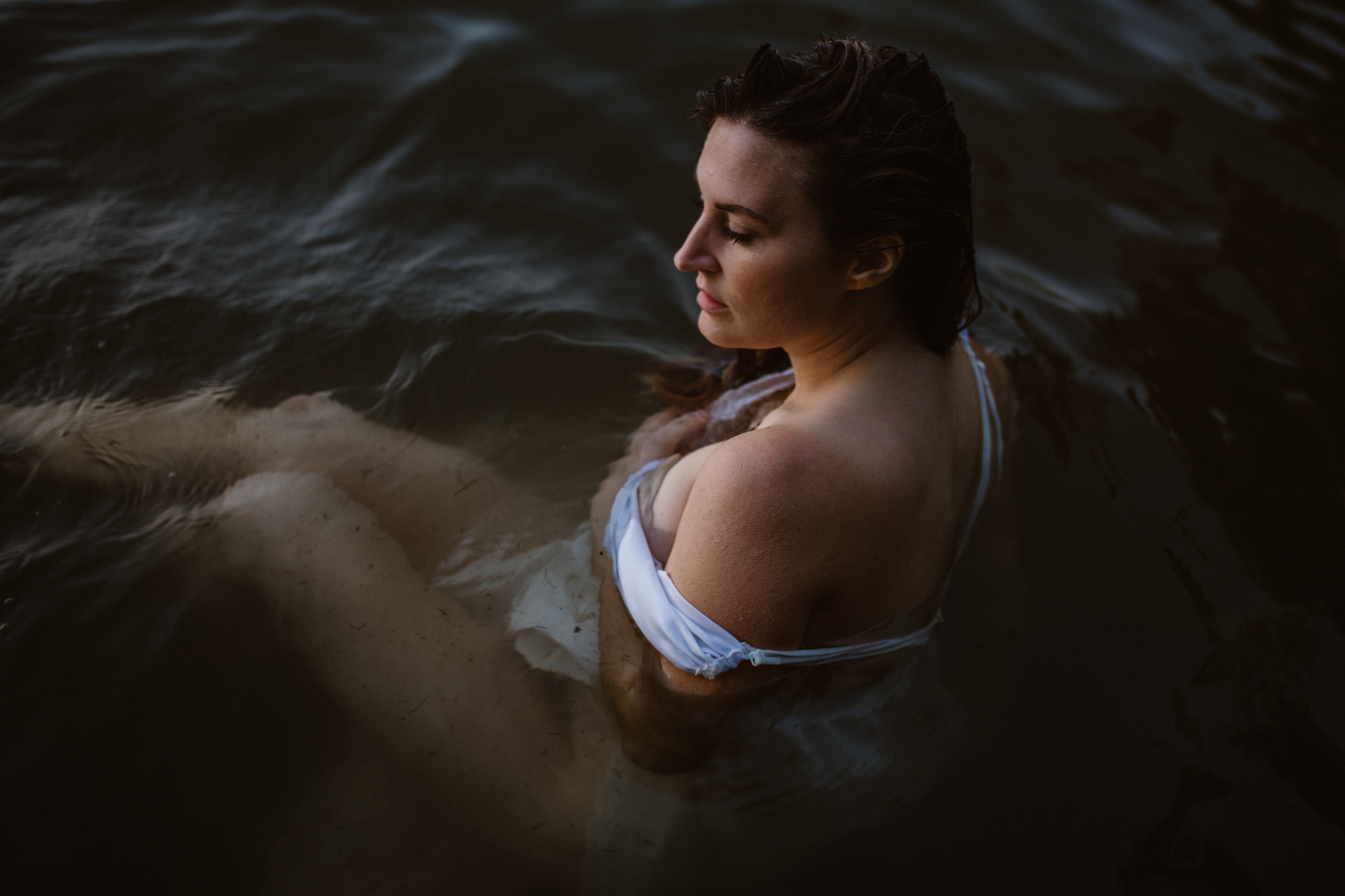 Woman in a white off the shoulder gown sitting the water with her eyes closed. Madison Wisconsin Boudoir.