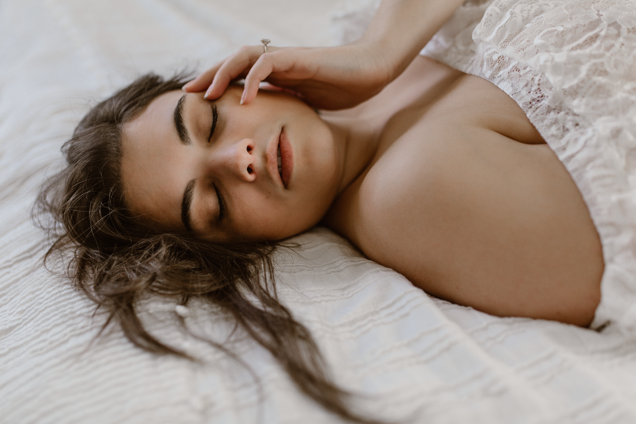 Woman on a bed with long hair, softly touching her face. Boudoir.