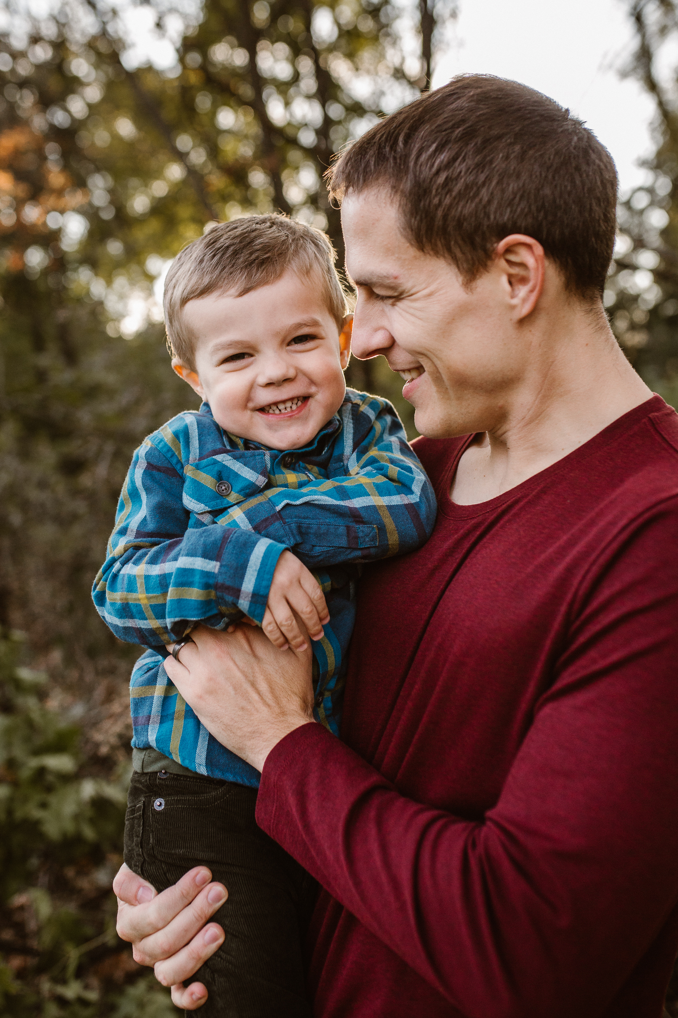 Father tickling his young son in the fall trees.