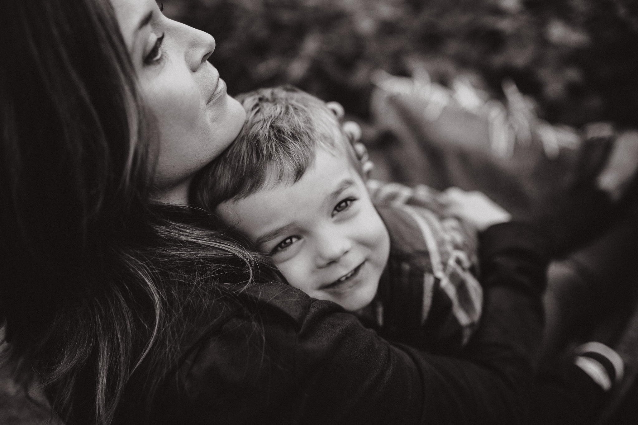 Young boy with his head pressed against his mohter's chest as she holds him.