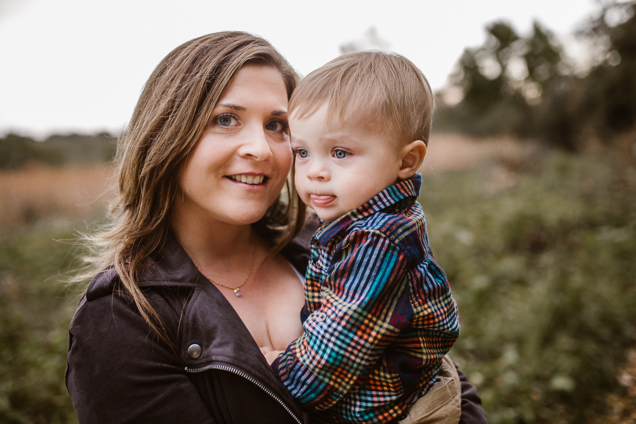 Mother holding her young son outside as he sticks his tongue out.