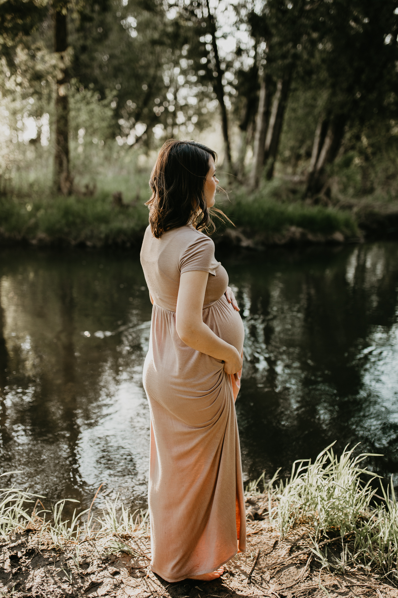 Expecting mother walking along the creek, pulling up her long dress.