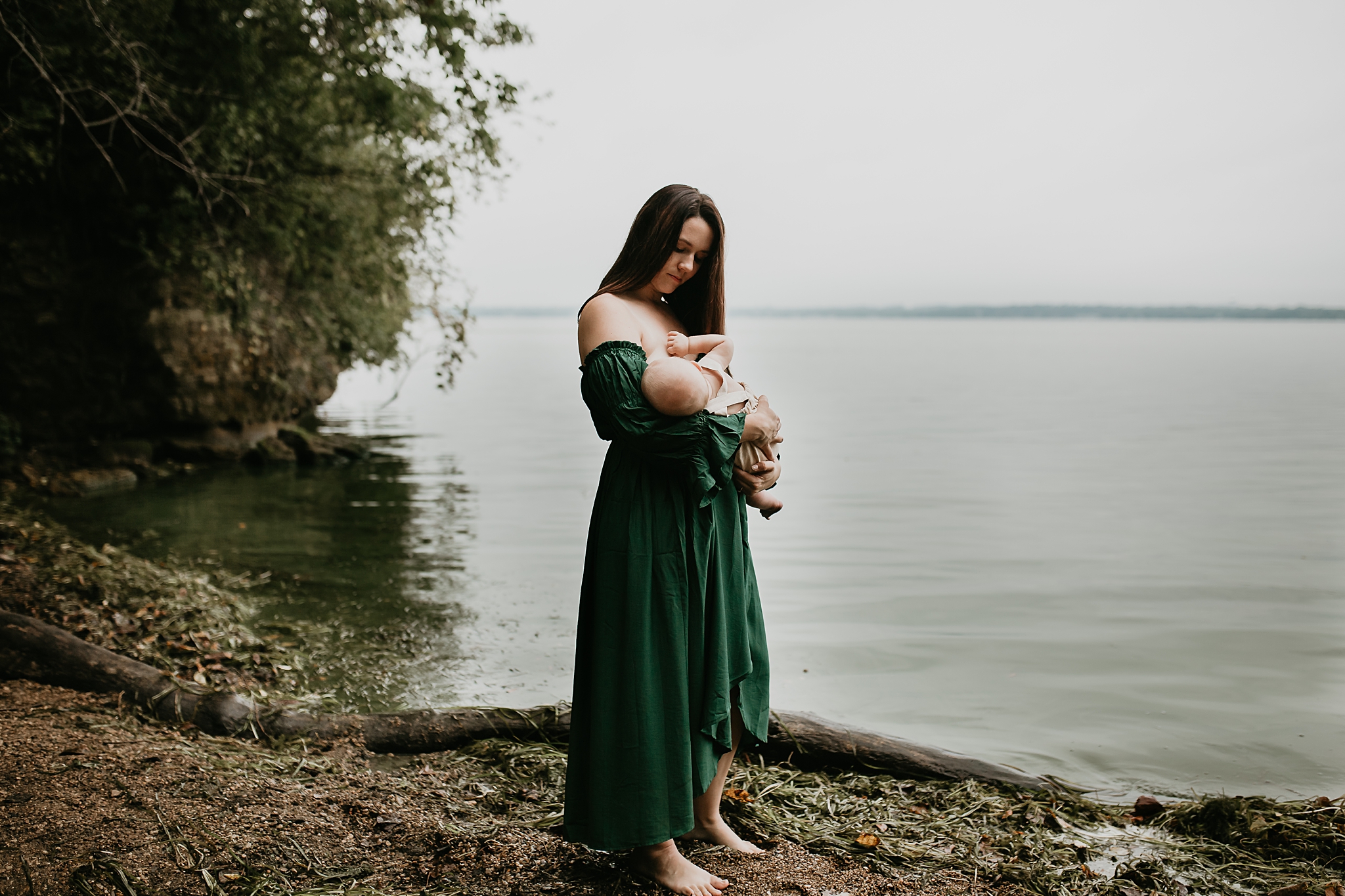 Mother breastfeeding her infant boy in a green dress by the lake.