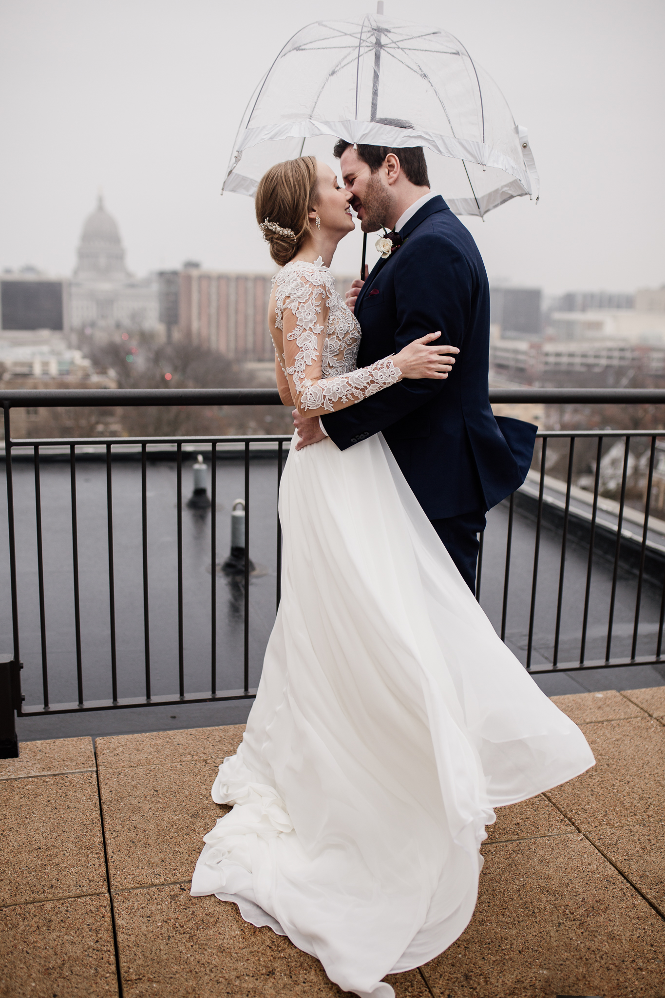 Bride and groom on the Edgewater Hotel balcony with an umbrella.
