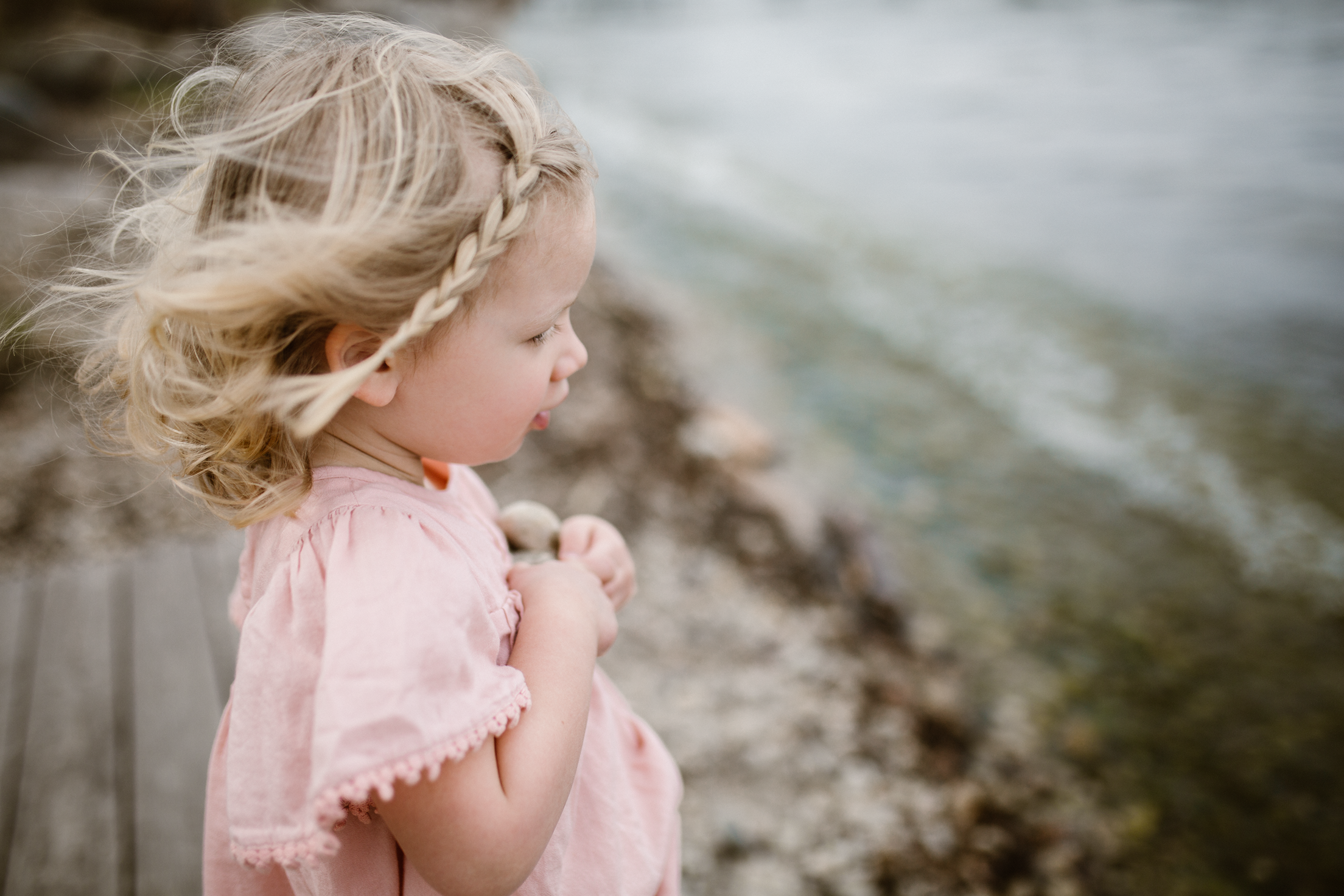Young girl in a pink dress holding rocks by the lake.