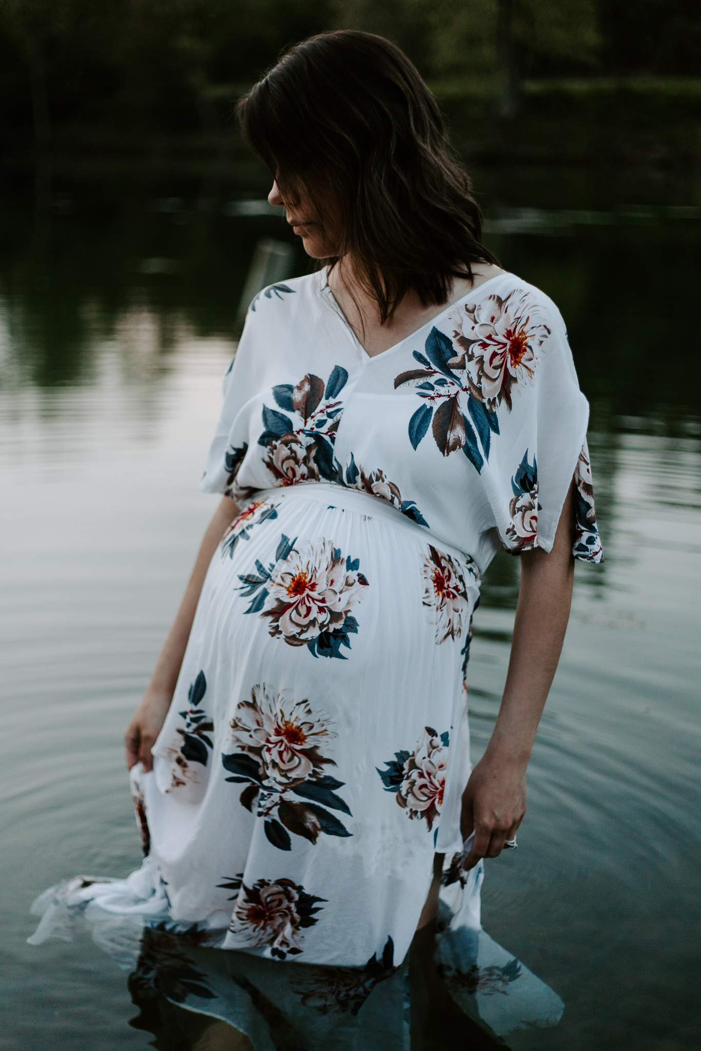Expecing mother in a floral maxi dress wading in pond at blue hour.