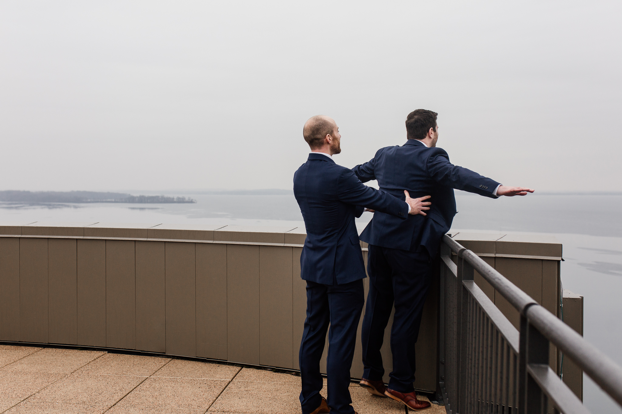 Best man holding groom by rooftop ledge doing Titanic pose.