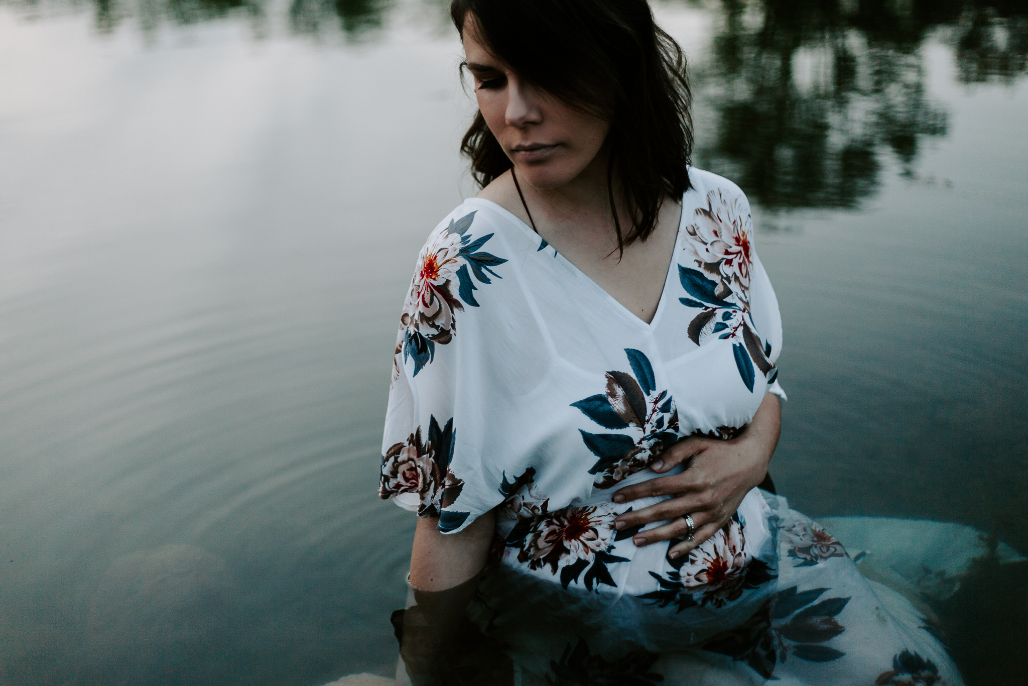 Expecing mother in a white floral dress sitting in pond at blue hour.