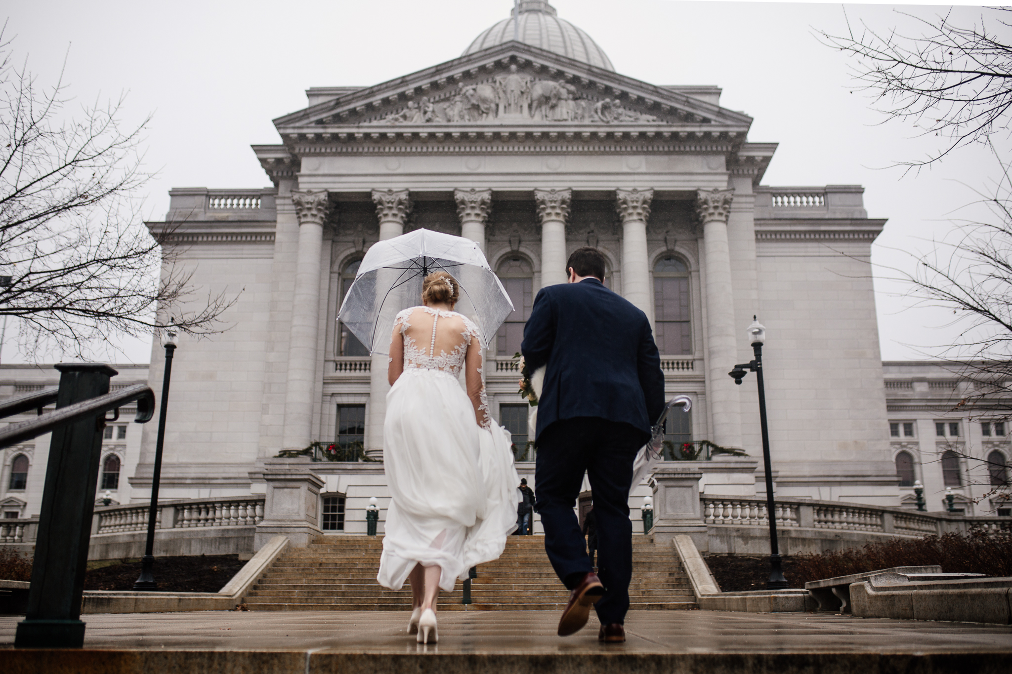 Bride and groom running up the Madison State Capitol stairs in the rain.