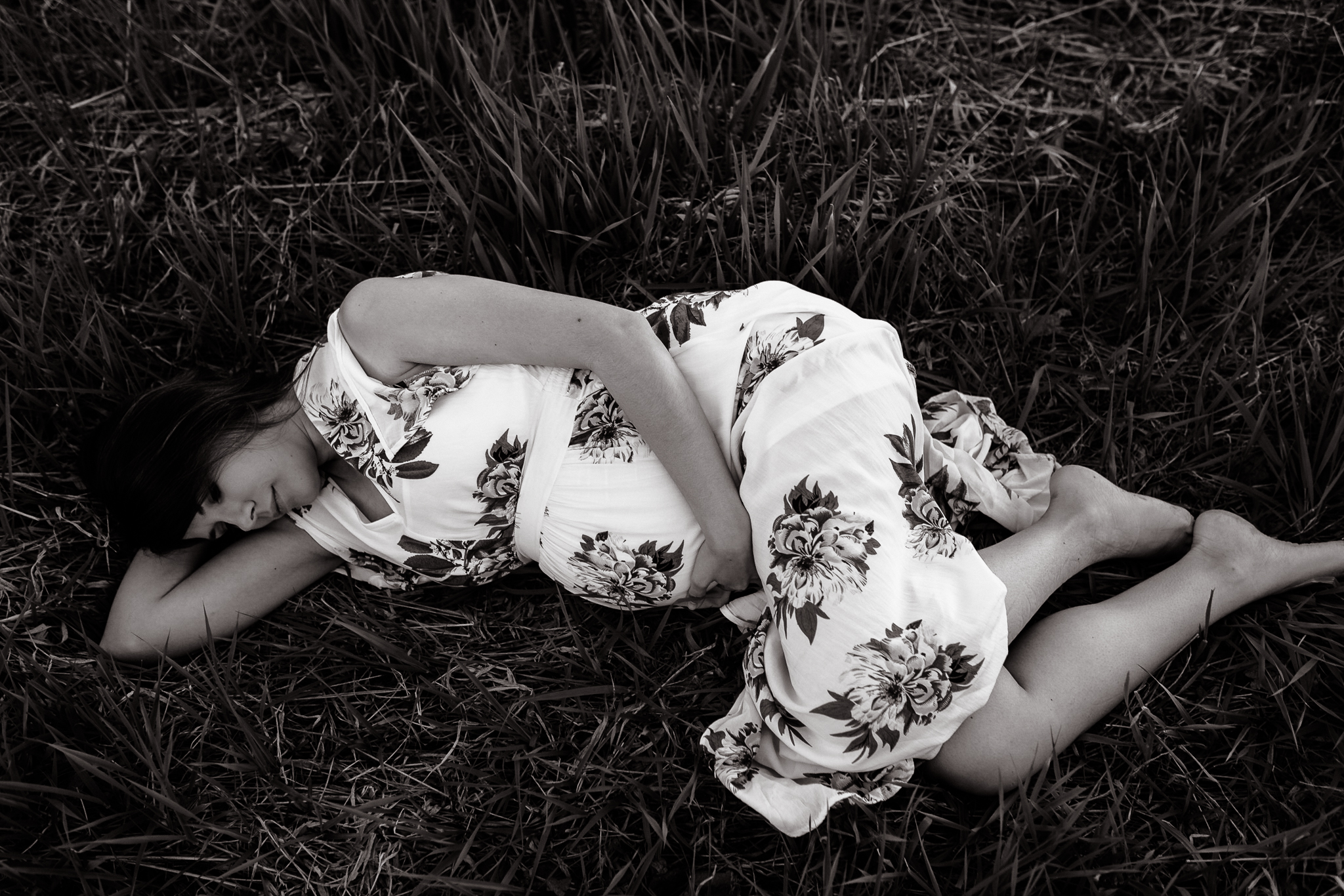 Expecting woman in a floral maxi dress laying down in a grass field.