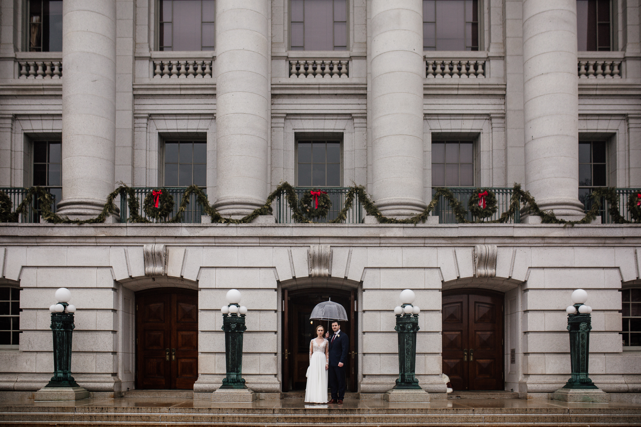Bride and groom standing with an umbrella in the doorway of the Madison State Capitol.