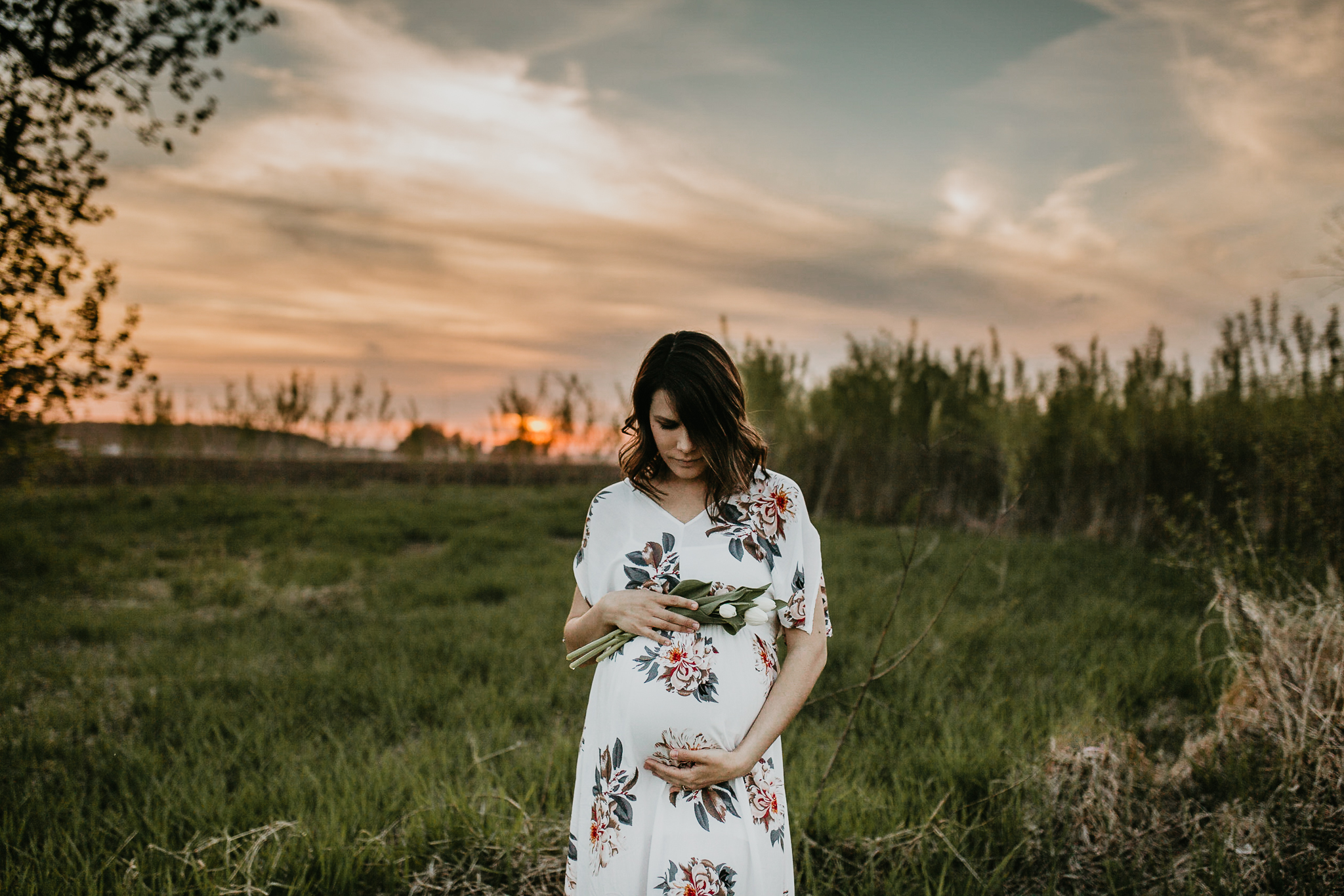 Pregnant mother in a field at golden hour looking down at her belly lovingly.