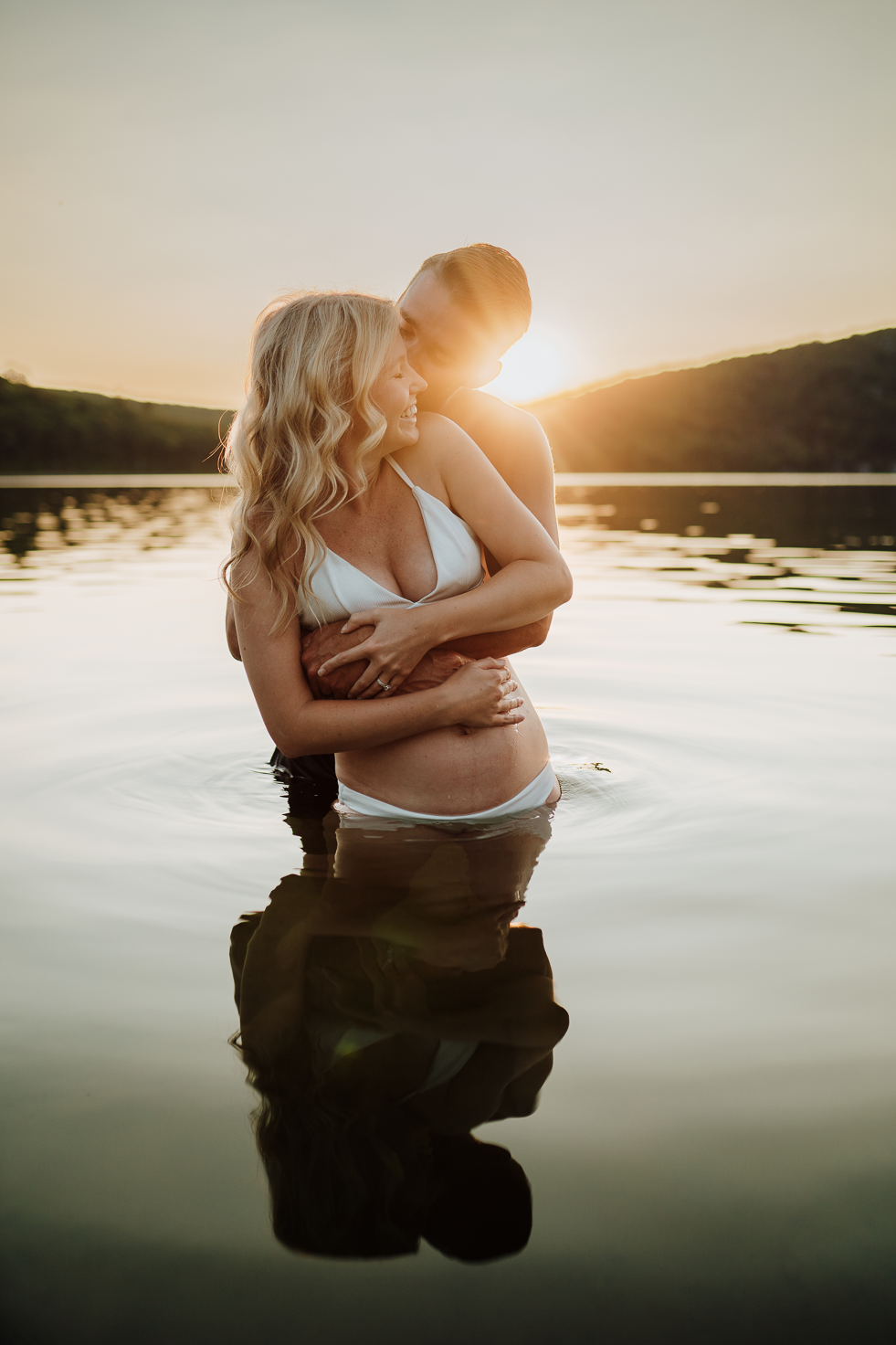 Husband holding his pregnant wife in the Wisconsin lake at sunset.