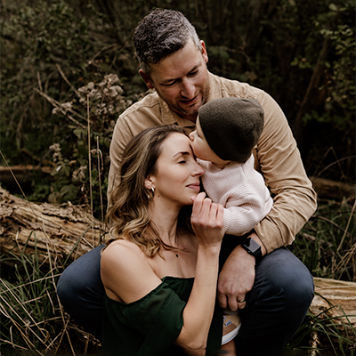 Baby boy kissing his mother's forehead while sitting on daddy.