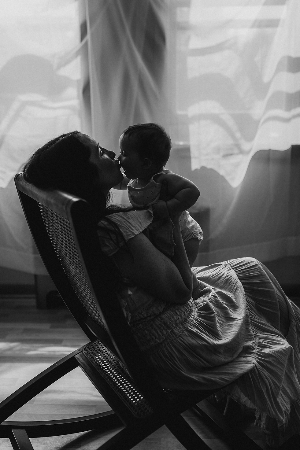 Madison motherhood photo session with a mother and baby kissing on a rocking chair in front of a window.
