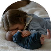 Toddler sister bending down to hug her new baby brother on a bed.
